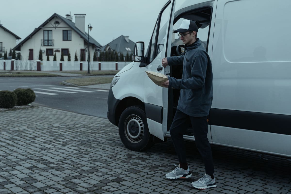 A driver with a parcel stepping out of a white van on a residential street