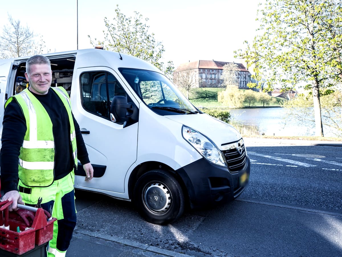 A worker in a hi-vis vest beside a white van, carrying a crate of tools